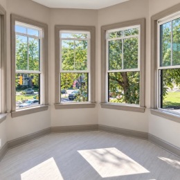 a corner of a room with wood flooring and several windows