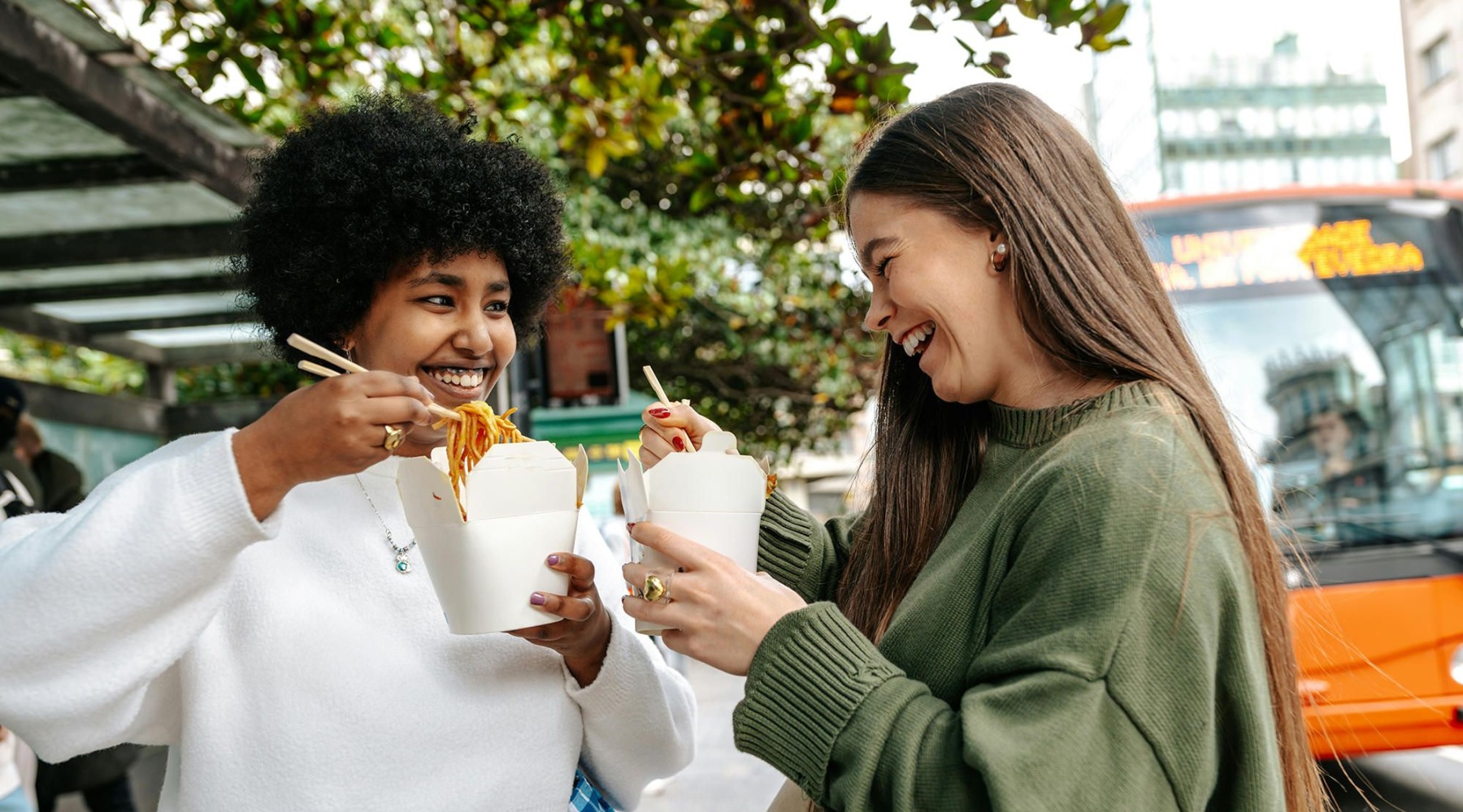 friends enjoying food together outside near an orange bus