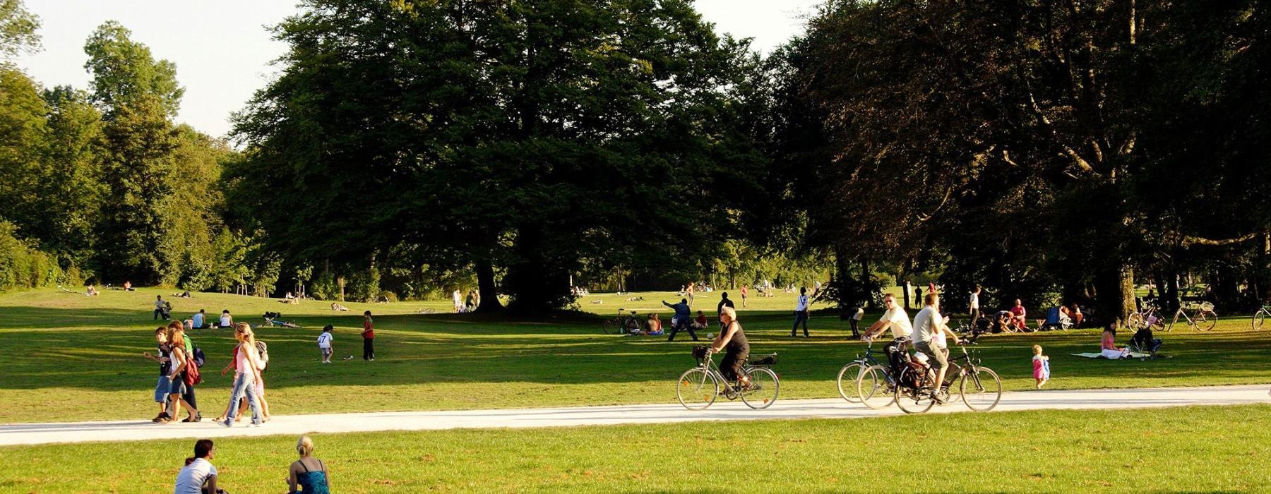 A park with many people riding bikes, having a picnic, and walking.